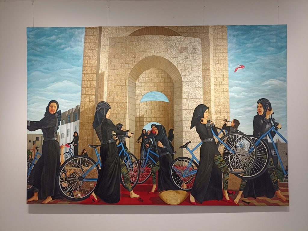 Photo d'un tableau de l'artiste Duaa Qishta qui représente des femmes devant une arche en pierre. Elles portent un voile noir et chacune porte un vélo.